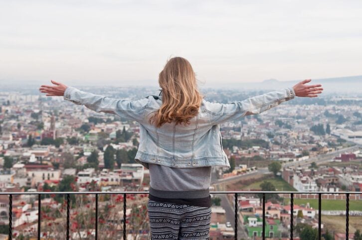 traveler woman with flying hair and raising hands looks at the landscape of Cholula, Mexico