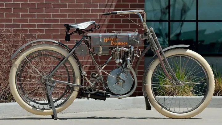 1908 gray motorcycle with orange Harley-Davidson lettering and off-white tires