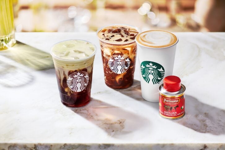 Starbucks Oleato Reserve beverages lineup on a wooden bar with small can of Partanna extra virgin olive oil