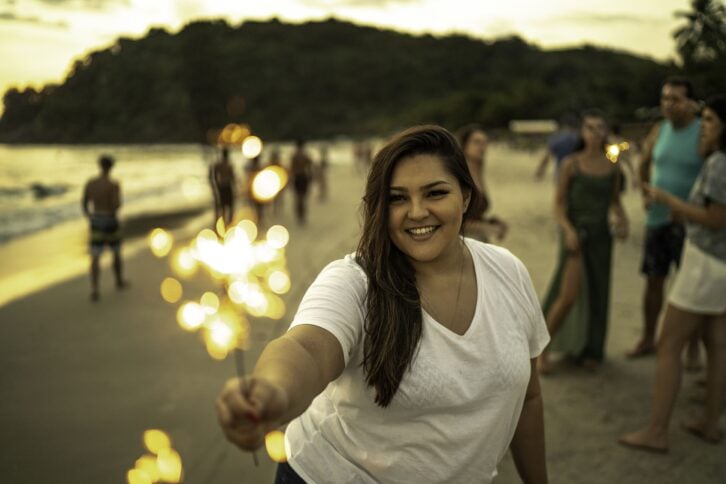young woman celebrating New Year with sparkler at beach