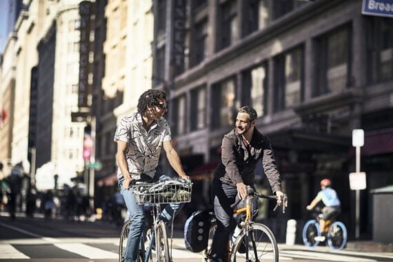 two smiling mid adult male friends riding bicycles on a sunny day in downtown Los Angeles