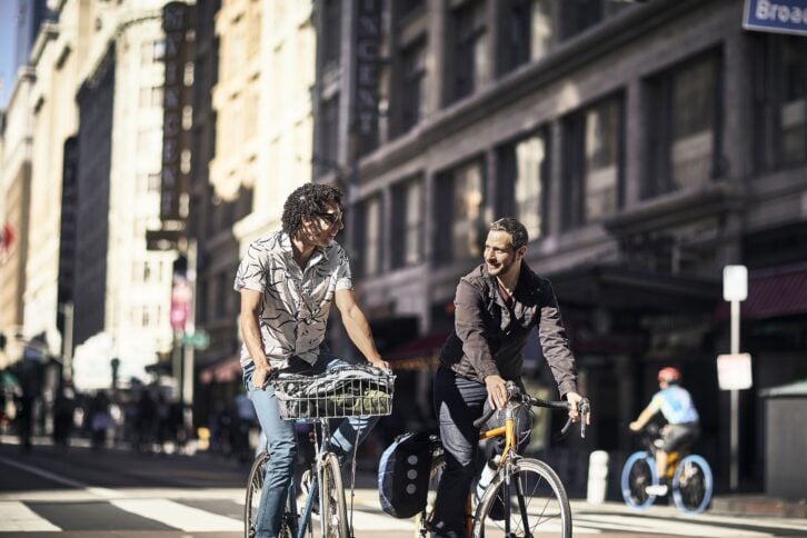 two smiling mid adult male friends riding bicycles on a sunny day in downtown Los Angeles