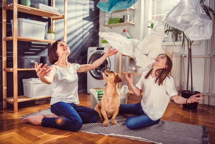 mother and daughter with small yellow dog sitting on the floor and throwing up clothes at laundry room