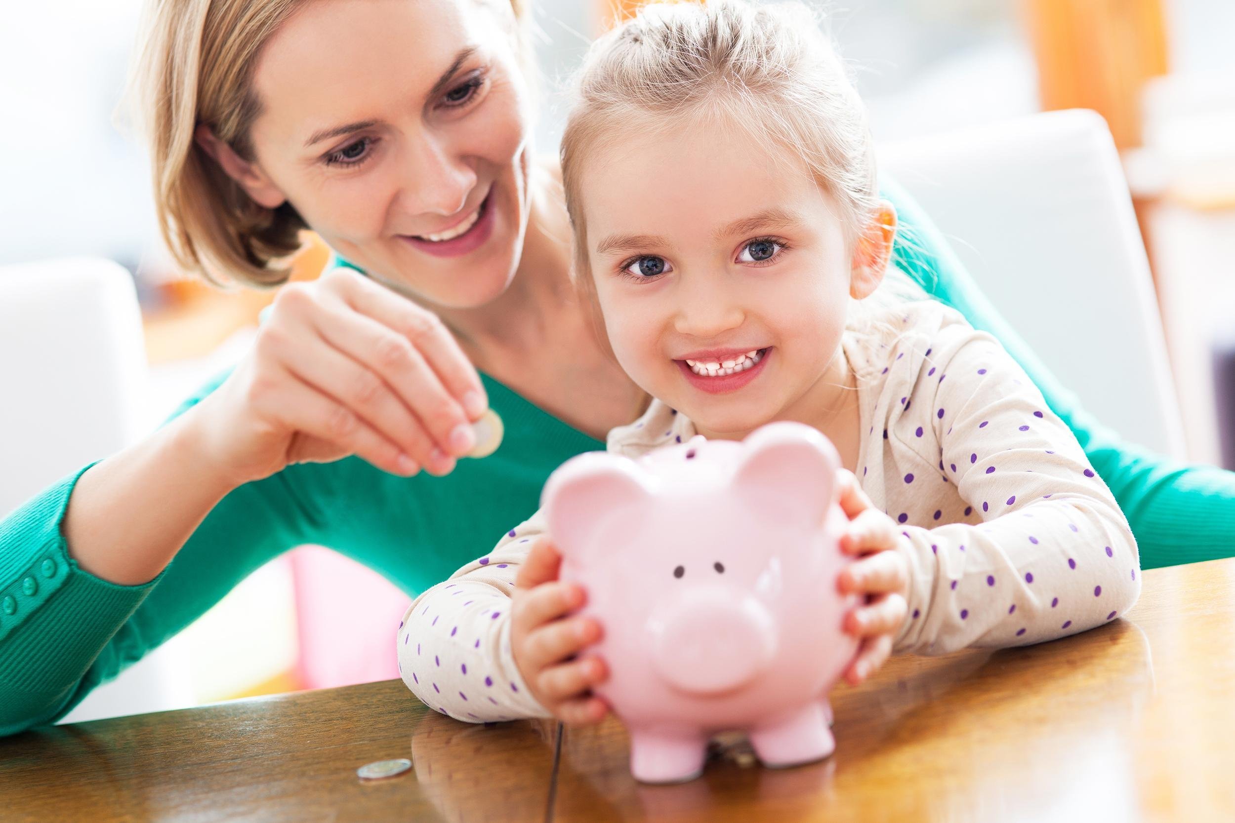 mother and daughter putting coins into piggy bank