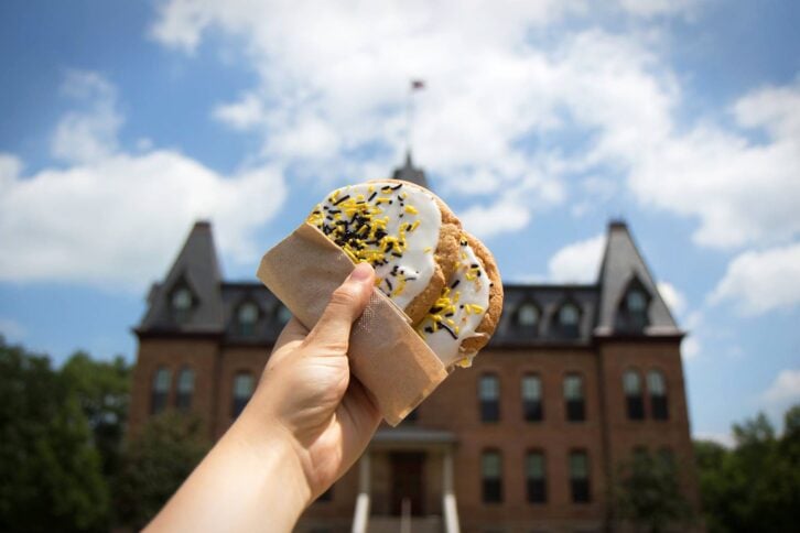Hand holding a cookie up to the sky with college in background