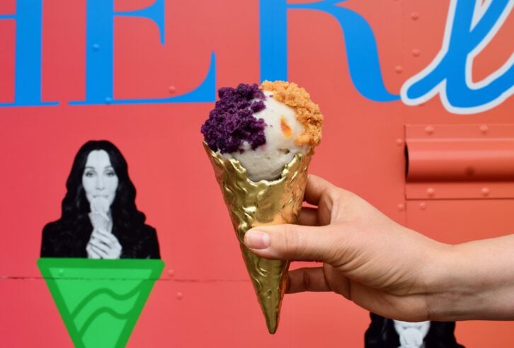 A hand holding a gold ice cream cone topped with gelato in front of the Cherlato food truck.