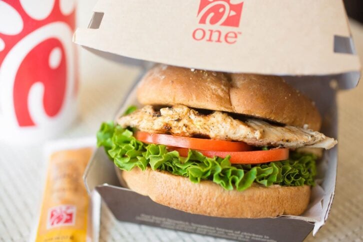 A close-up shot of the Chick-fil-A Grilled Chicken Sandwich in a cardboard container with a sauce packet.