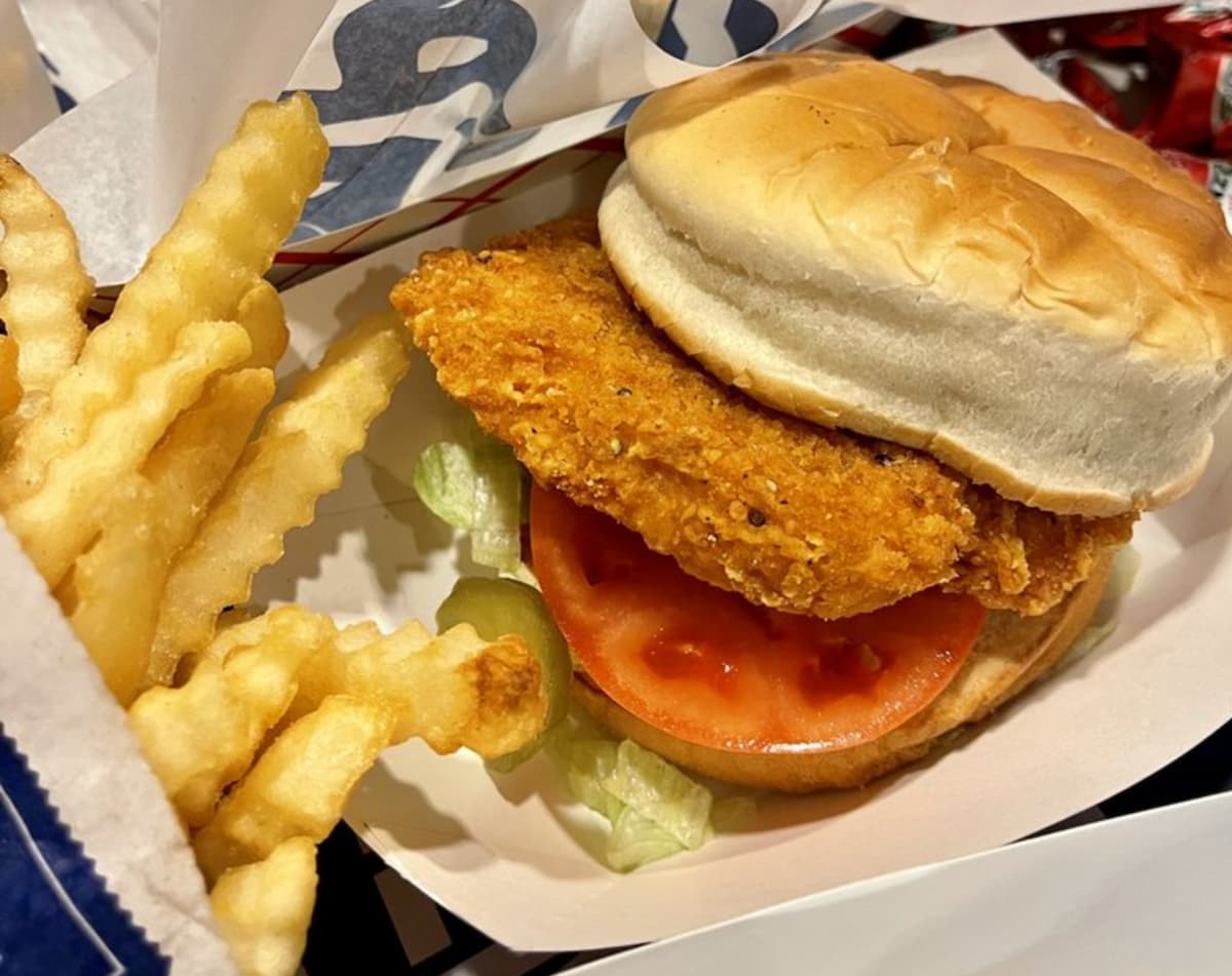 A close-up of a crispy fried chicken sandwich with lettuce and tomato on a soft bun, served next to crinkle-cut French fries in a paper tray—just like the classics at fast-food chains with real chicken.