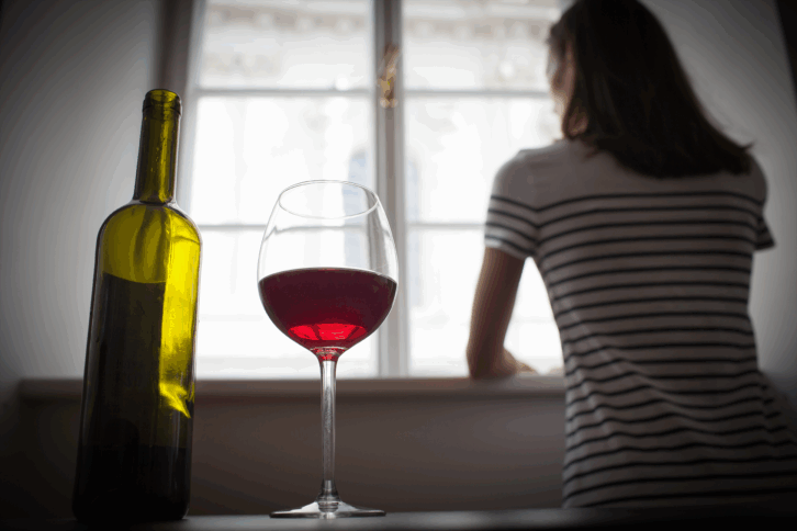 Woman standing by window with wine and bottle in foreground