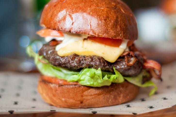Closeup of easy juicy air fryer hamburger with lettuce, tomato, and cheese toppings on white and black polka dot paper with blurred background