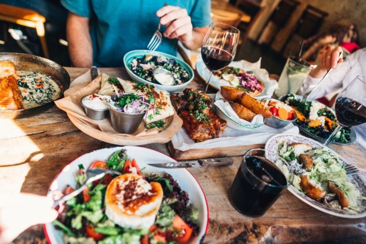 Focus on food at a Mediterranean restaurant on a rustic wooden table with a group of friends with a blurred background