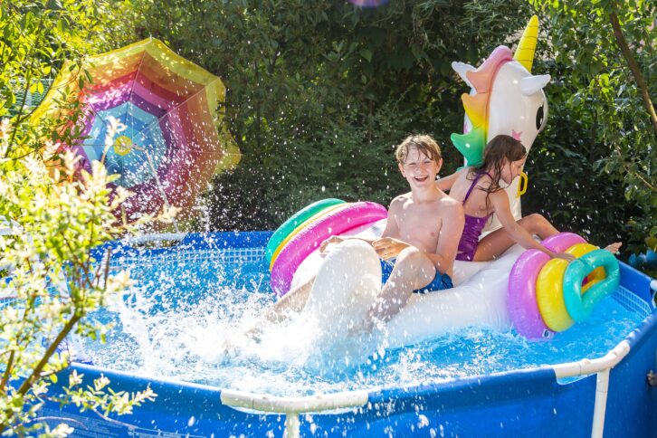 Brother and sister with oversized unicorn swim toy in above-ground pool