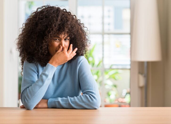 An African American woman in a blue top is holding her nose and making a face due to something stinky.