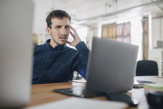 A man looks incredibly confused while viewing a laptop monitor.