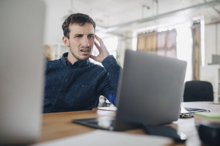 A man looks incredibly confused while viewing a laptop monitor.