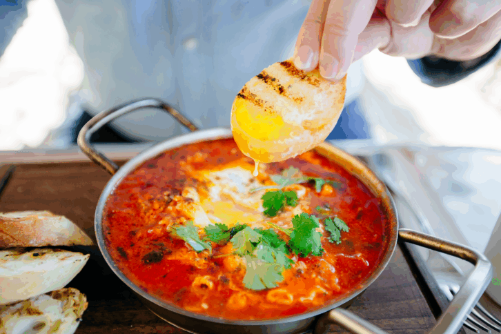 Dipping fresh bread in shakshuka, close up