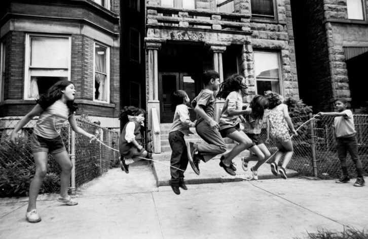 A black and white photo of six children jump a rope held by two others in Chicago in 1970s.