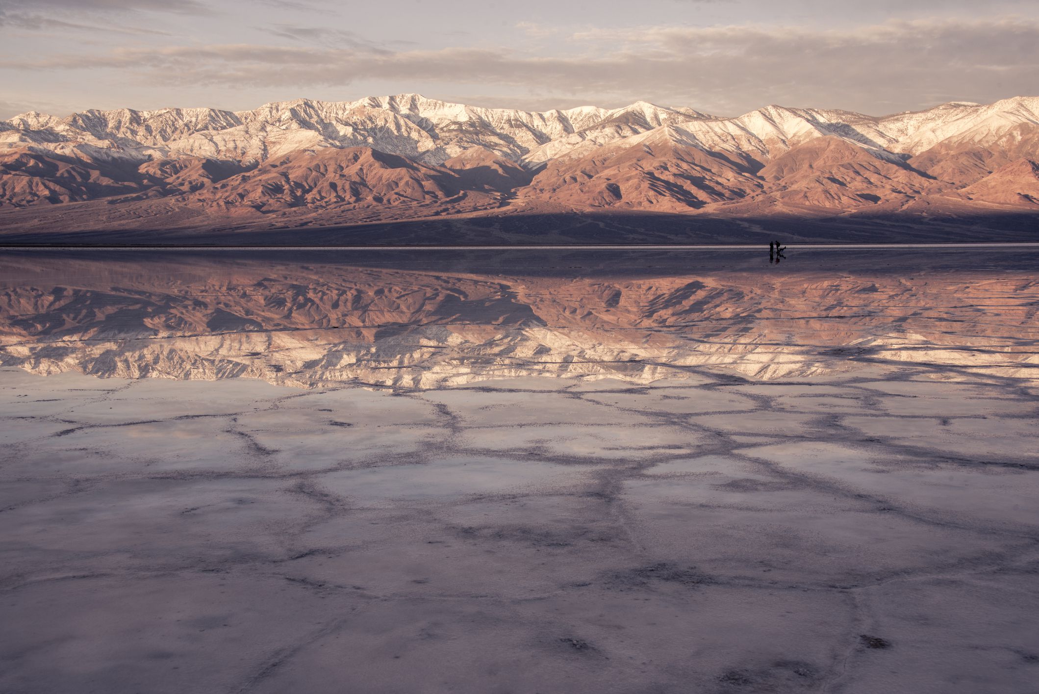 The Panamint mountain range at Badwater basin at sunrise in Death Valley reflected in temporary winter lake with salt polygons visible