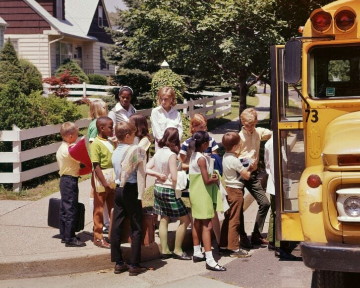 1960s 1970s Ethnically Diverse Group Of School Kids Boys And Girls Getting On A School Bus In A Suburban Neighborhood