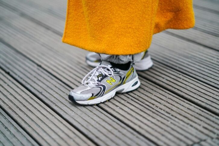 Ellie Delphine wears an orange wool coat, New Balance sneakers shoes, on January 06, 2021 in Paris, France