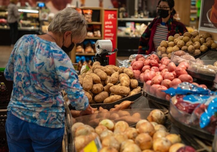 woman shopping in grocery store June 2022 looking at potatoes in produce section
