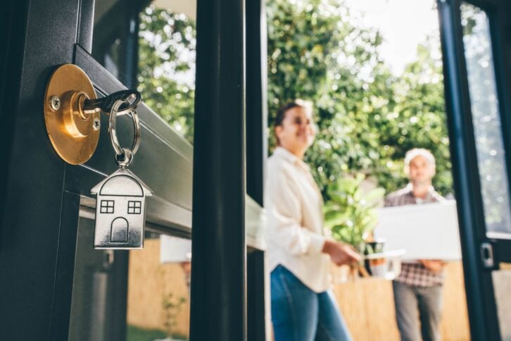 A couple stands outside a door with a new house key in it