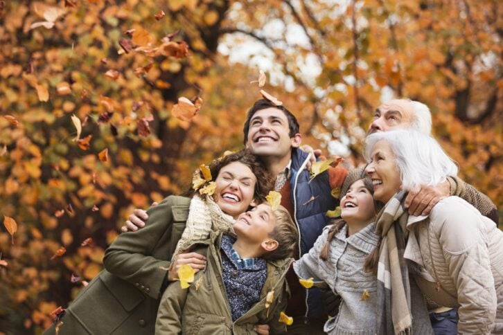 family playing in autumn leaves in park