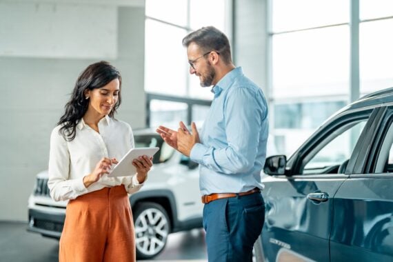 Cheerful car dealership customer talking to auto sales consultant