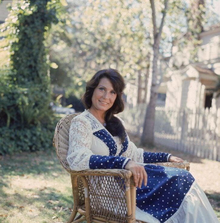 Portrait of American country music singer and guitarist Loretta Lynn as she sits outside in a chair, 1970s.