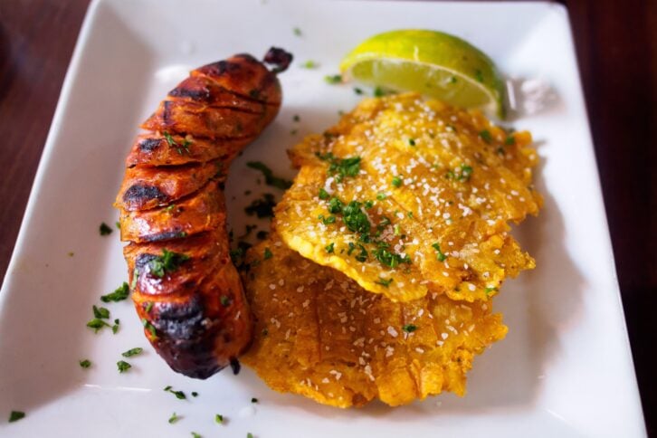 tostones, salchicha and lime on plate with sprinkled herbs