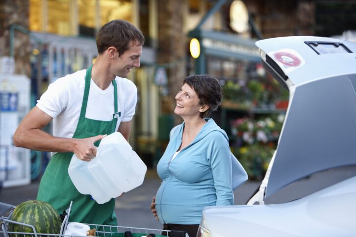 supermarket employee packing curbside pickup customer's trunk with groceries