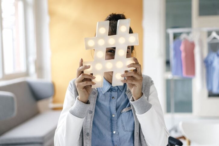 young woman hiding behind hashtag sign in studio