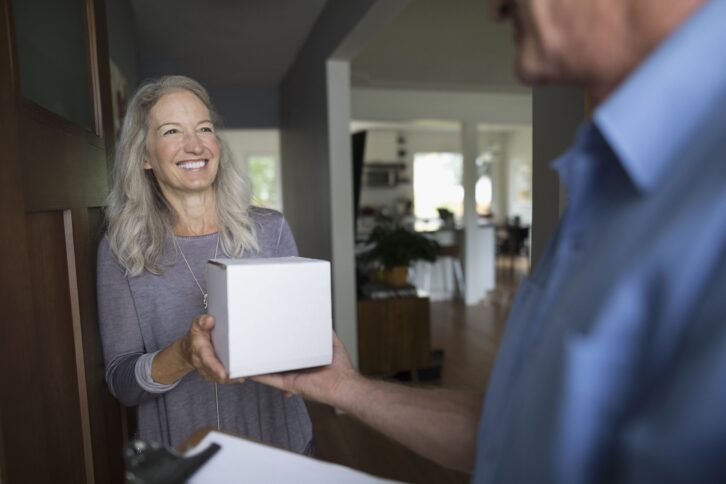 smiling senior woman receiving box package from delivery man at front door