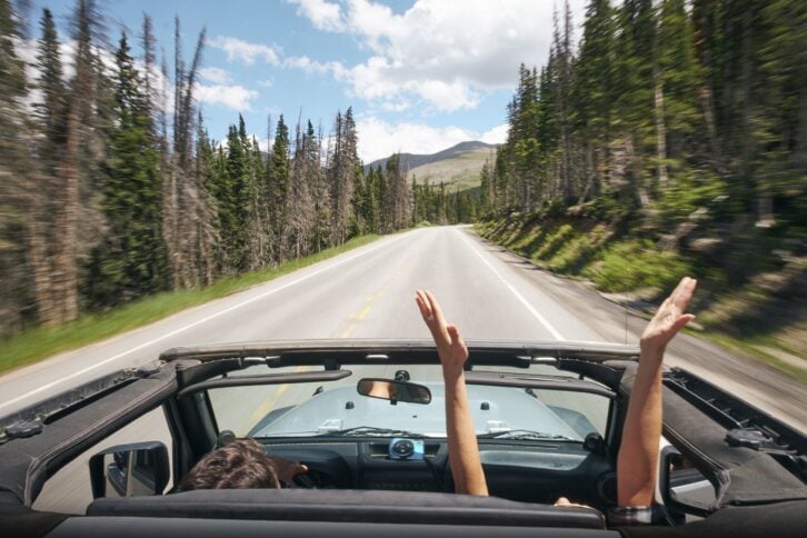 road trip couple driving convertible on rural highway with hands raised, Breckenridge, Colorado
