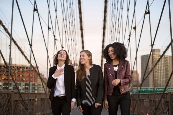 Cheerful friends walking on Brooklyn Bridge against clear sky