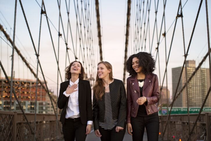 Cheerful friends walking on Brooklyn Bridge against clear sky
