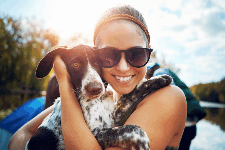 Woman smiling and holding her dog outside in the sunshine