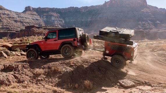 Red Jeep towing a Jeep trailer off road with mountains in the background