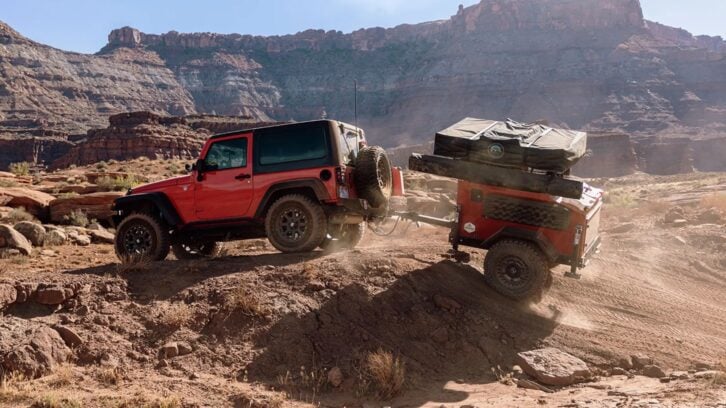 Red Jeep towing a Jeep trailer off road with mountains in the background