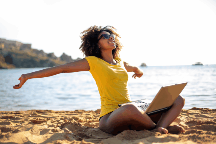 Happy woman working on her laptop on the beach