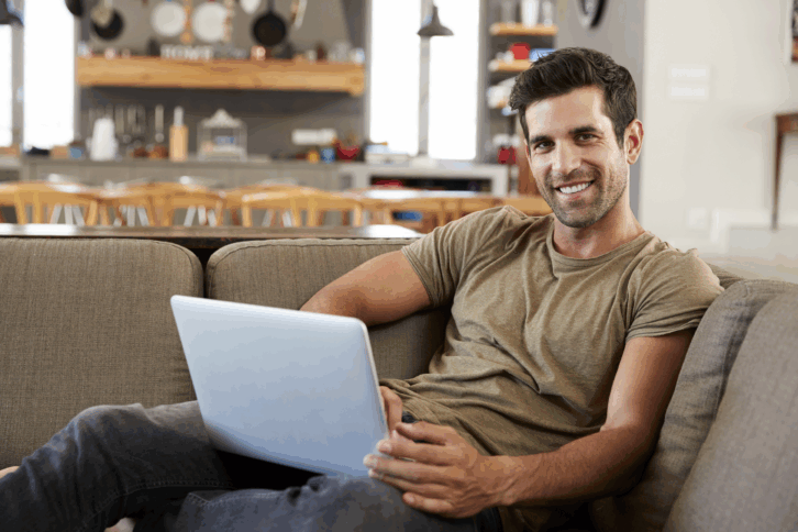 Smiling man working on his laptop from his couch