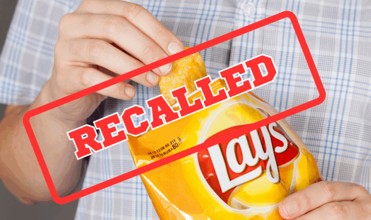 Tambov, Russian Federation - January 20, 2013: Hand takes out potato chip from Lay's bag. It is a potato chips with cheese. Recall sign on top