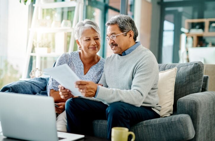 Middle-aged couple going through paperwork together at home, both sitting on the couch in living room, woman is looking happily at her husband