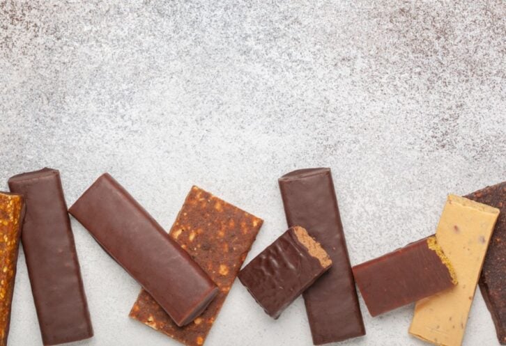 Nine opened protein bars scattered in a line on the bottom half of the image on a silvery table