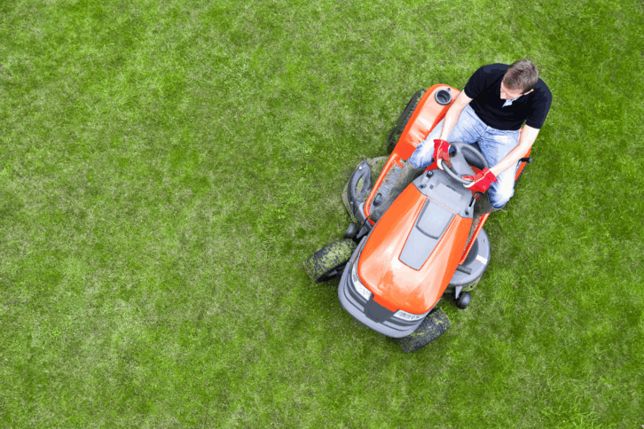 Overhead shot of man on orange riding lawn mower cutting grass, on right side, bright green grass in image