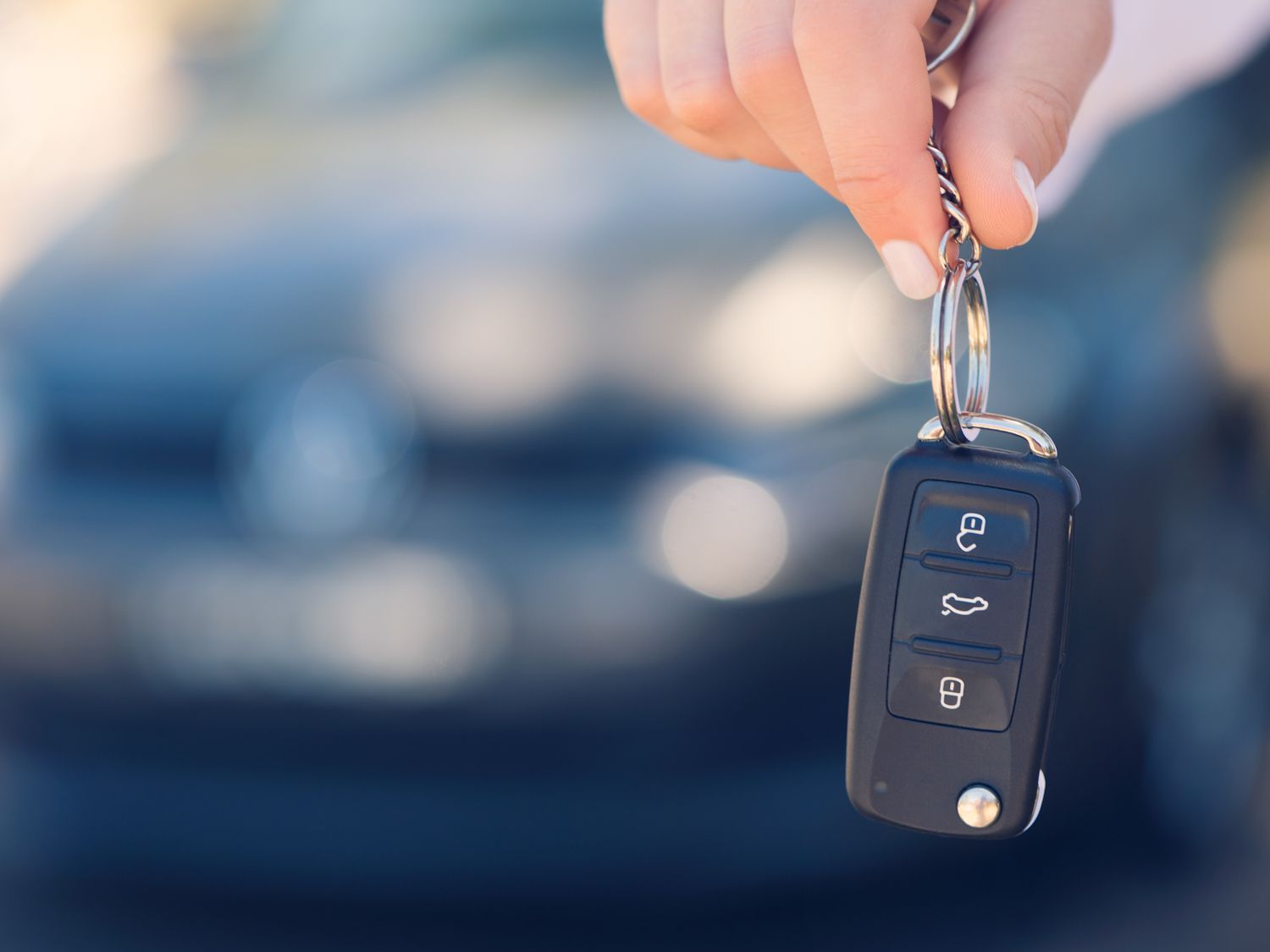 Female car salesperson handing over the new car keys. There is a new car behind her out of focus. Close up with Copy space