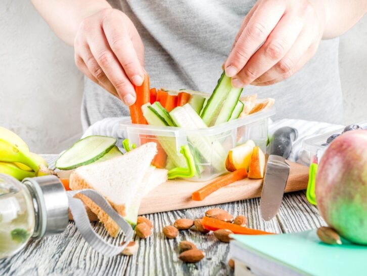 Mother cooking school lunch box set, Preparing healthy snacks-cheese sandwich with cucumber, carrot. Nuts, fruits and vegetable in box.