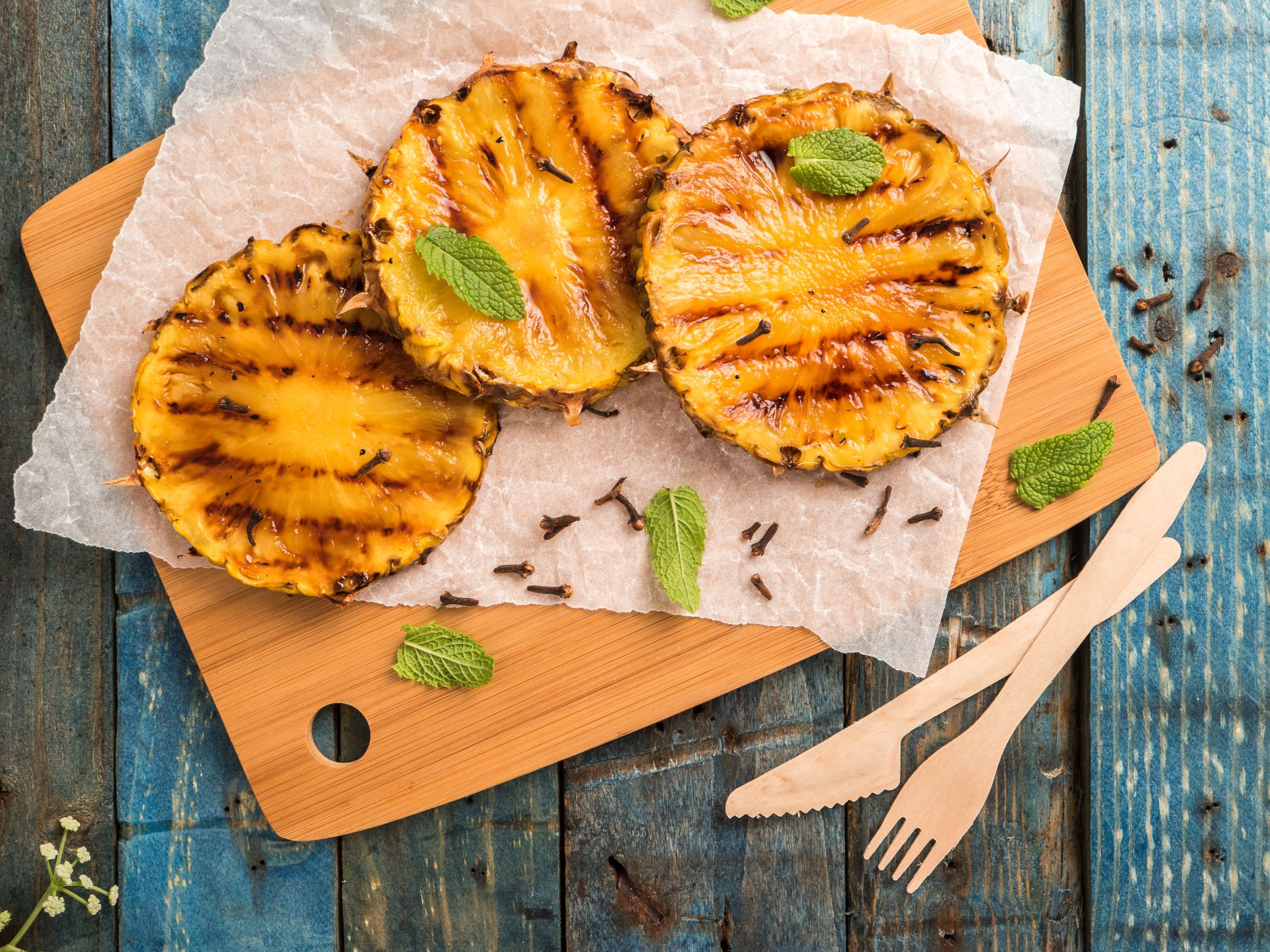 three slices of grilled pineapple on a wooden cutting board garnished with mint leaves