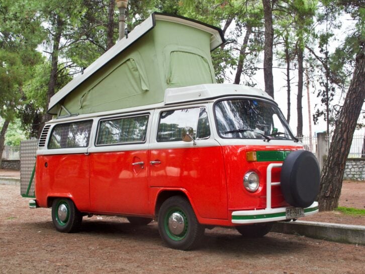 A loaded up vintage, orange and white Volkswagen bus is parked at a resting point during a road trip