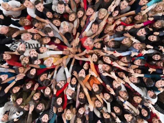 High angle view of large group of happy people joining hands in unity and looking at camera.